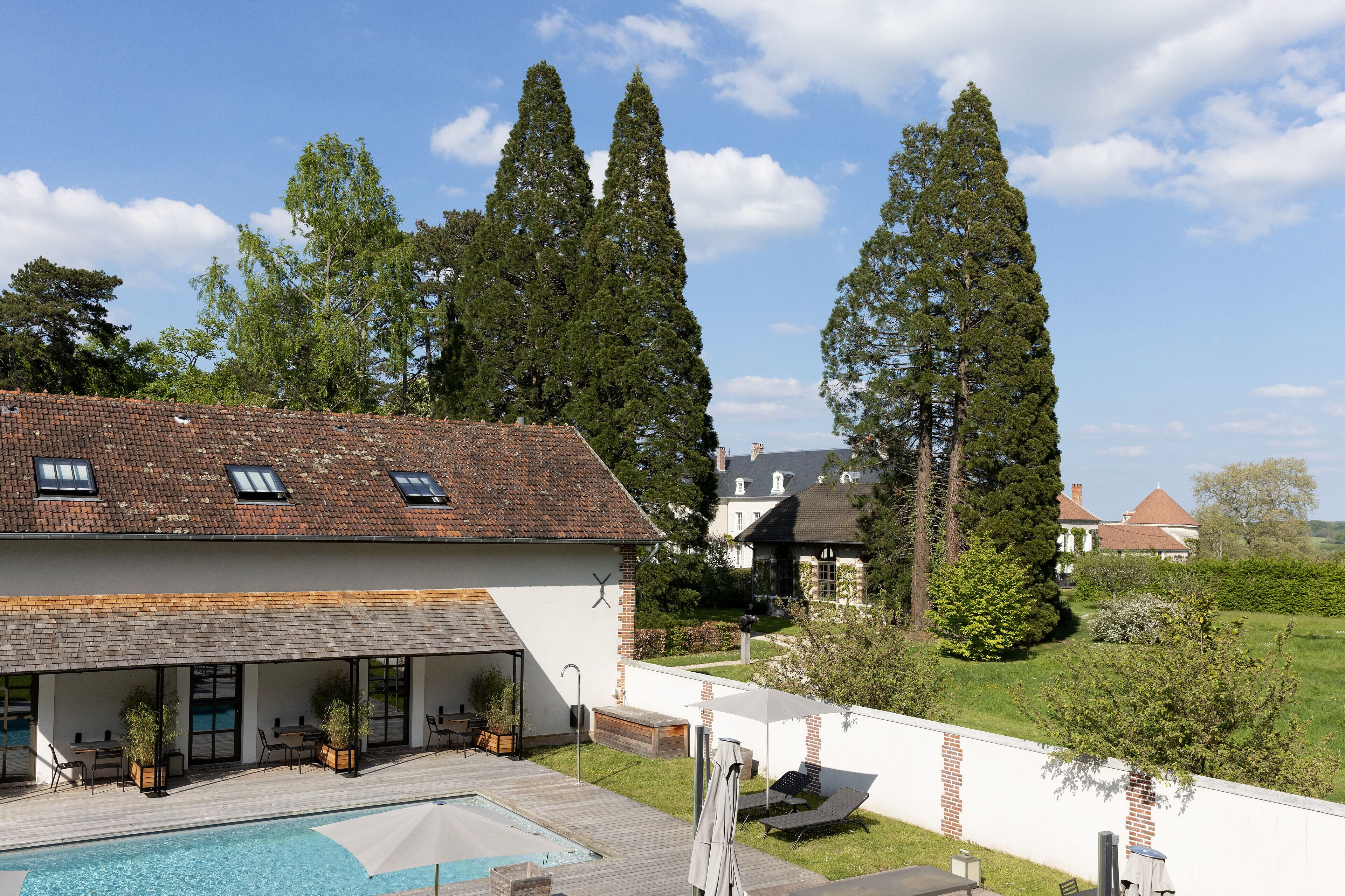 A modern house with a swimming pool, outdoor seating, and tall trees in the background.