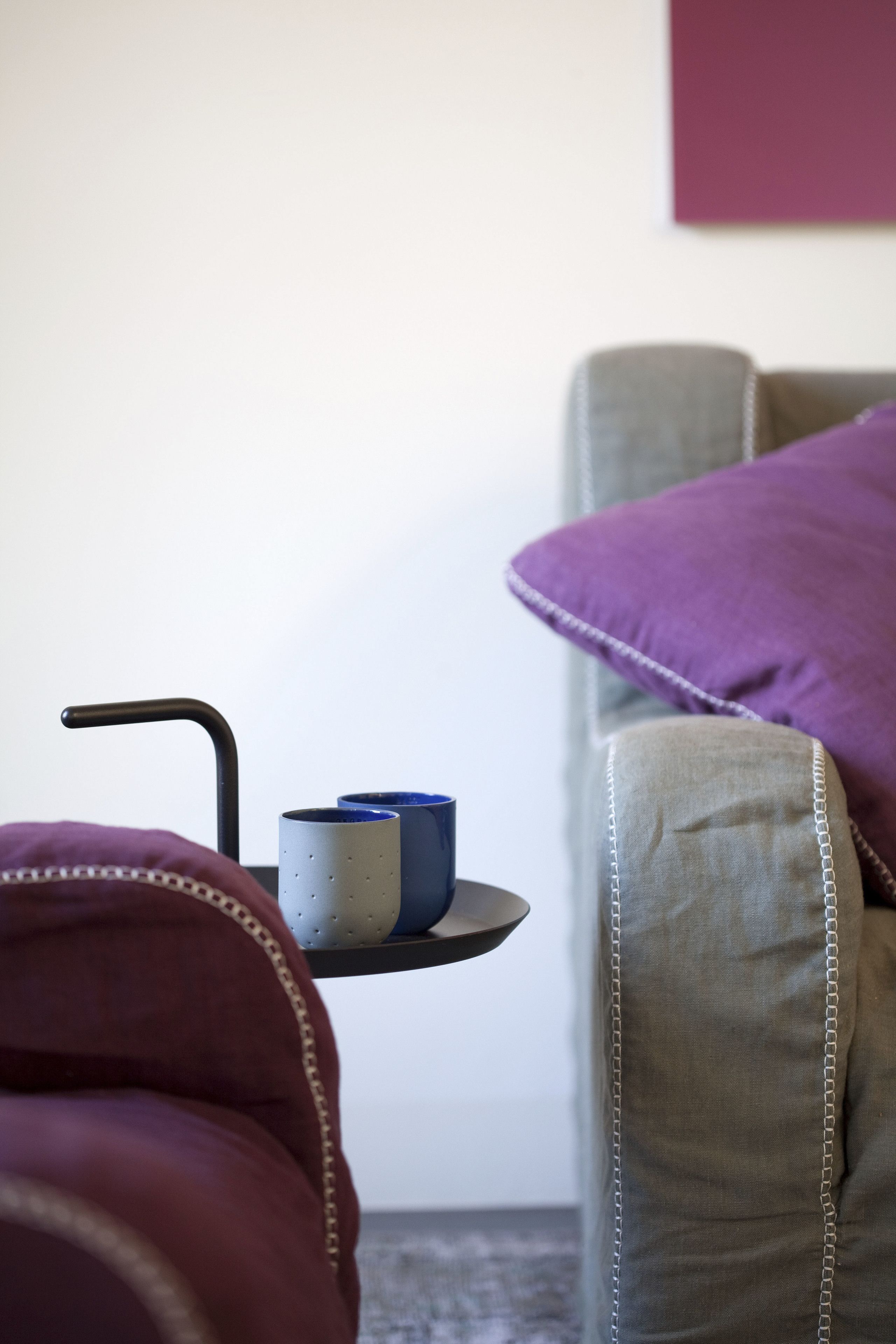 Ein modernes Wohnzimmer mit einem grauen Sofa, einem violetten Kissen und einem kleinen Tisch mit zwei Tassen.