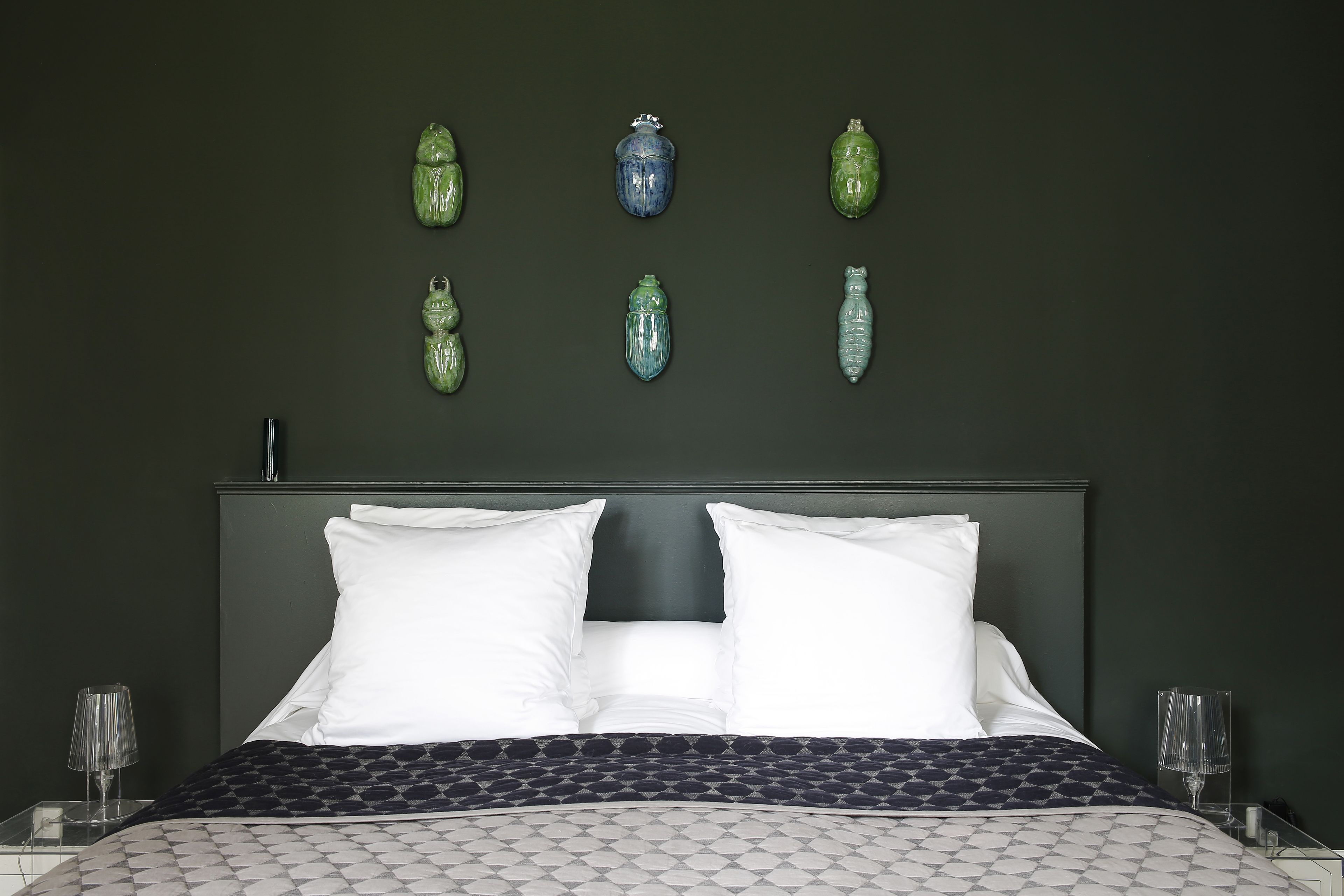 A neatly made bed with white and patterned bedding, a dark headboard, and decorative vases on the wall.