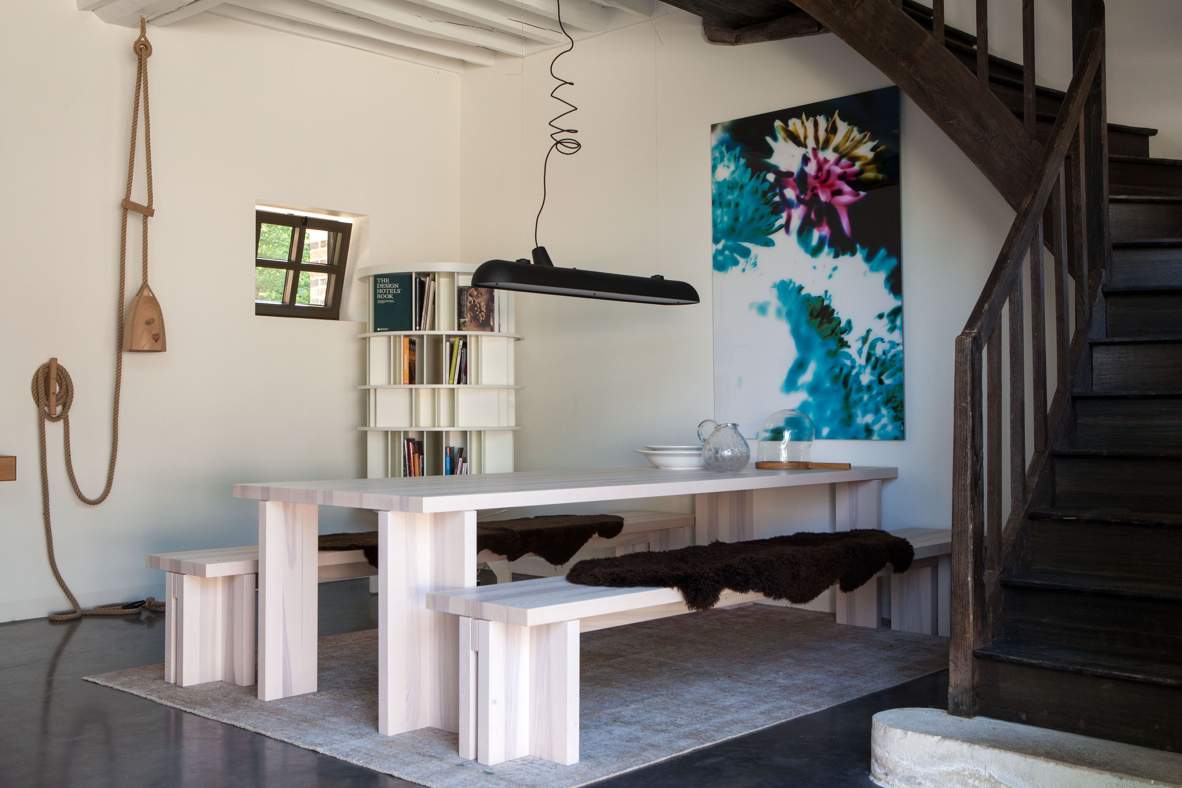 Un interior moderno con una mesa de madera, estanterías, un cuadro y una escalera.