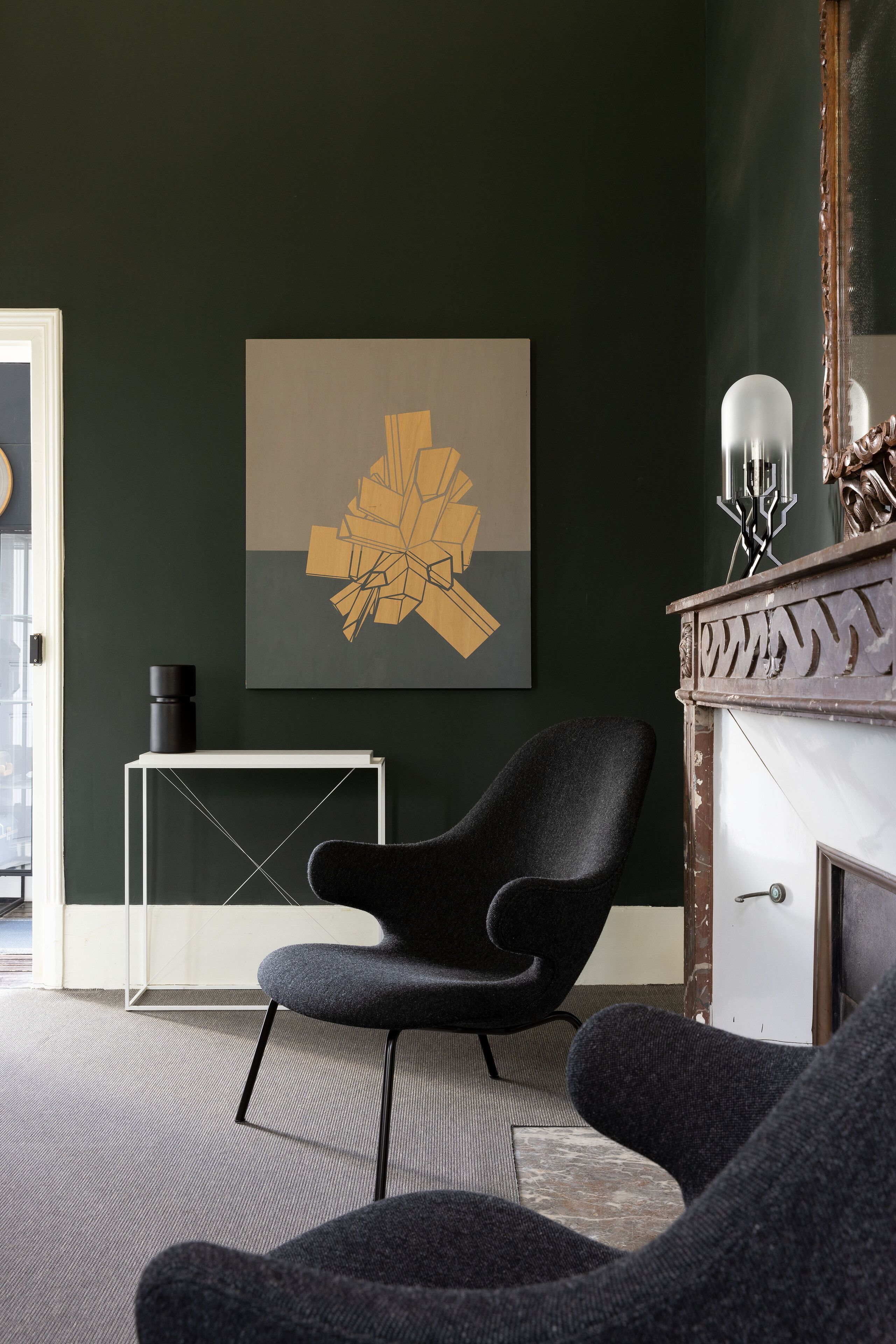 Una habitación moderna con una pared verde oscuro, un sillón negro, una consola blanca y una obra de arte abstracta enmarcada.