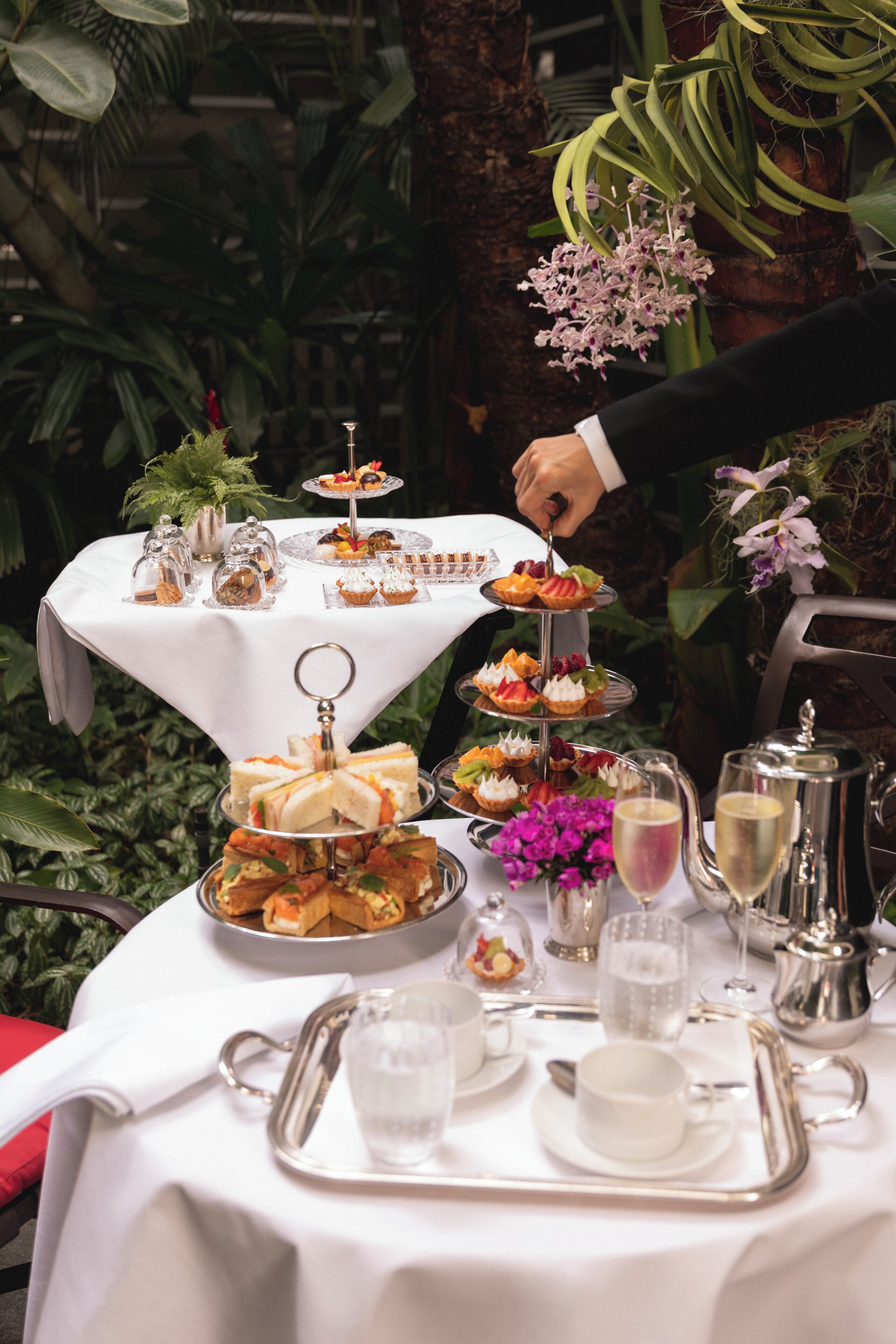 Une table dressée avec une variété de plats, notamment des sandwichs, des pâtisseries et des desserts, disposés sur une nappe blanche.