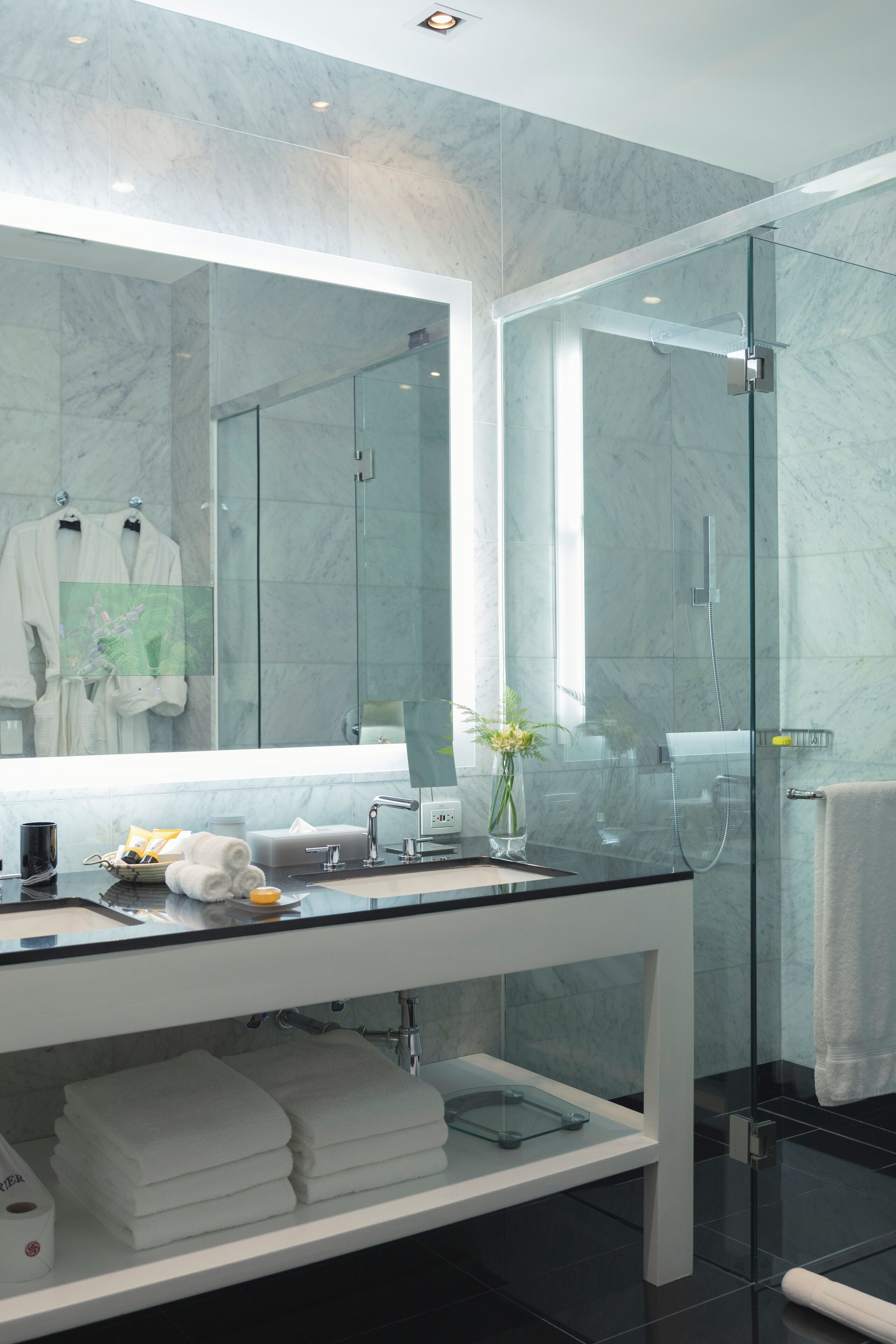 Une salle de bain moderne dotée d’une douche à parois de verre, d’un grand miroir et d’un meuble-lavabo avec un plan de travail en marbre.