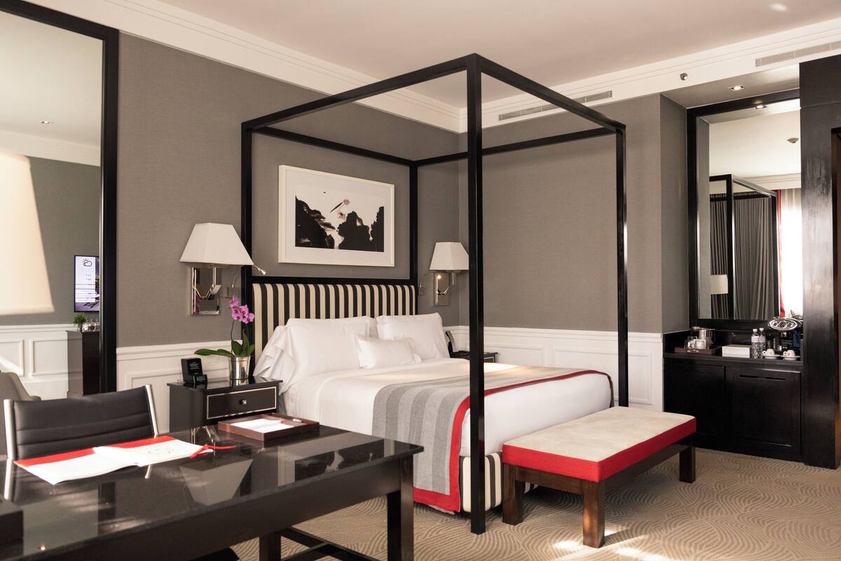 Une chambre d’hôtel avec un lit à baldaquin, des tables de chevet, un bureau et un grand miroir.