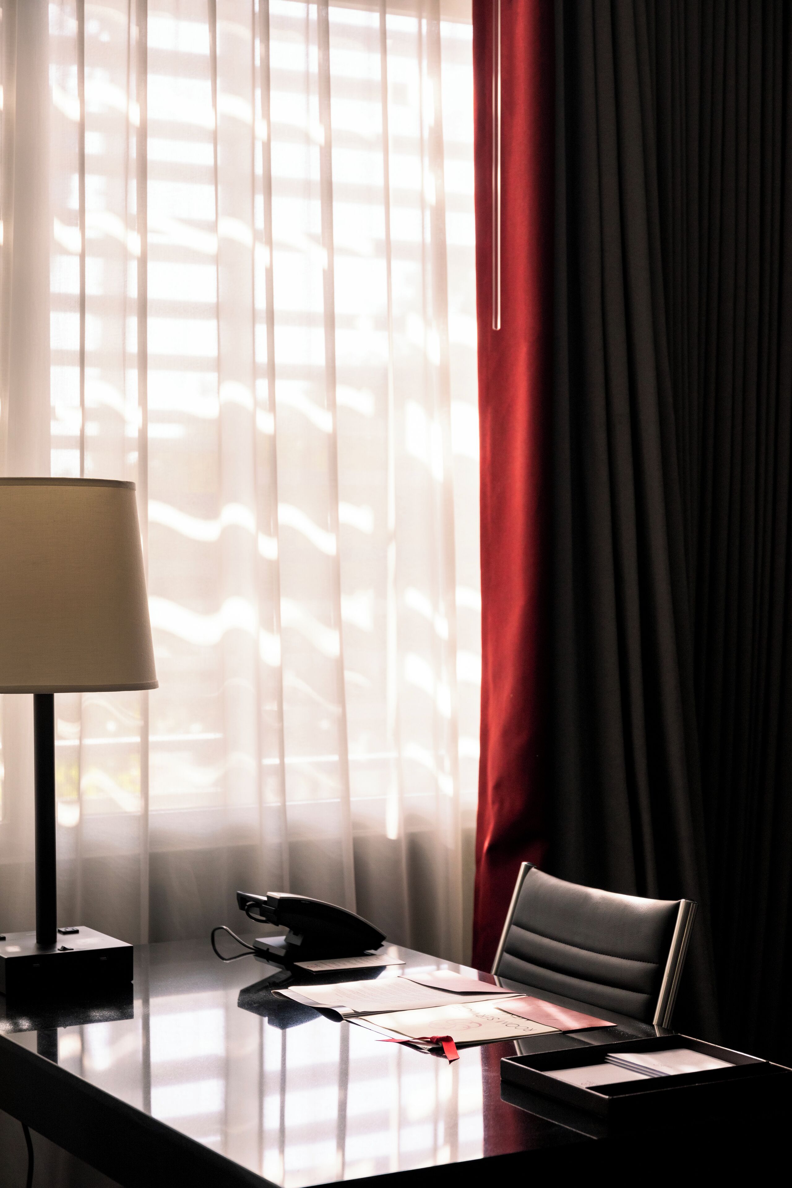 A hotel room with a desk, a lamp, a telephone, and a chair.