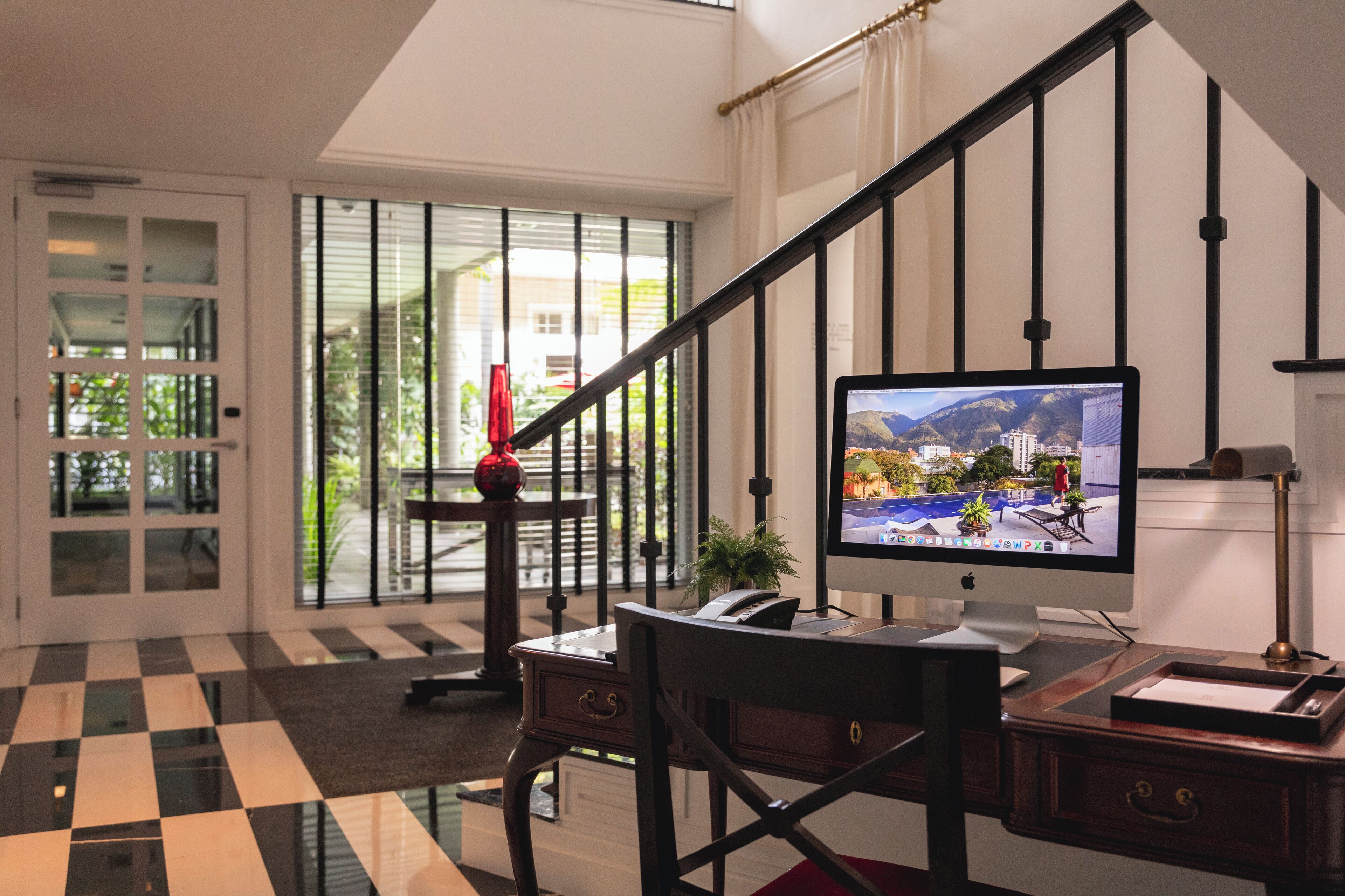 A modern hotel room with a checkered floor, a desk with a computer, a staircase, and a view of the outdoors.