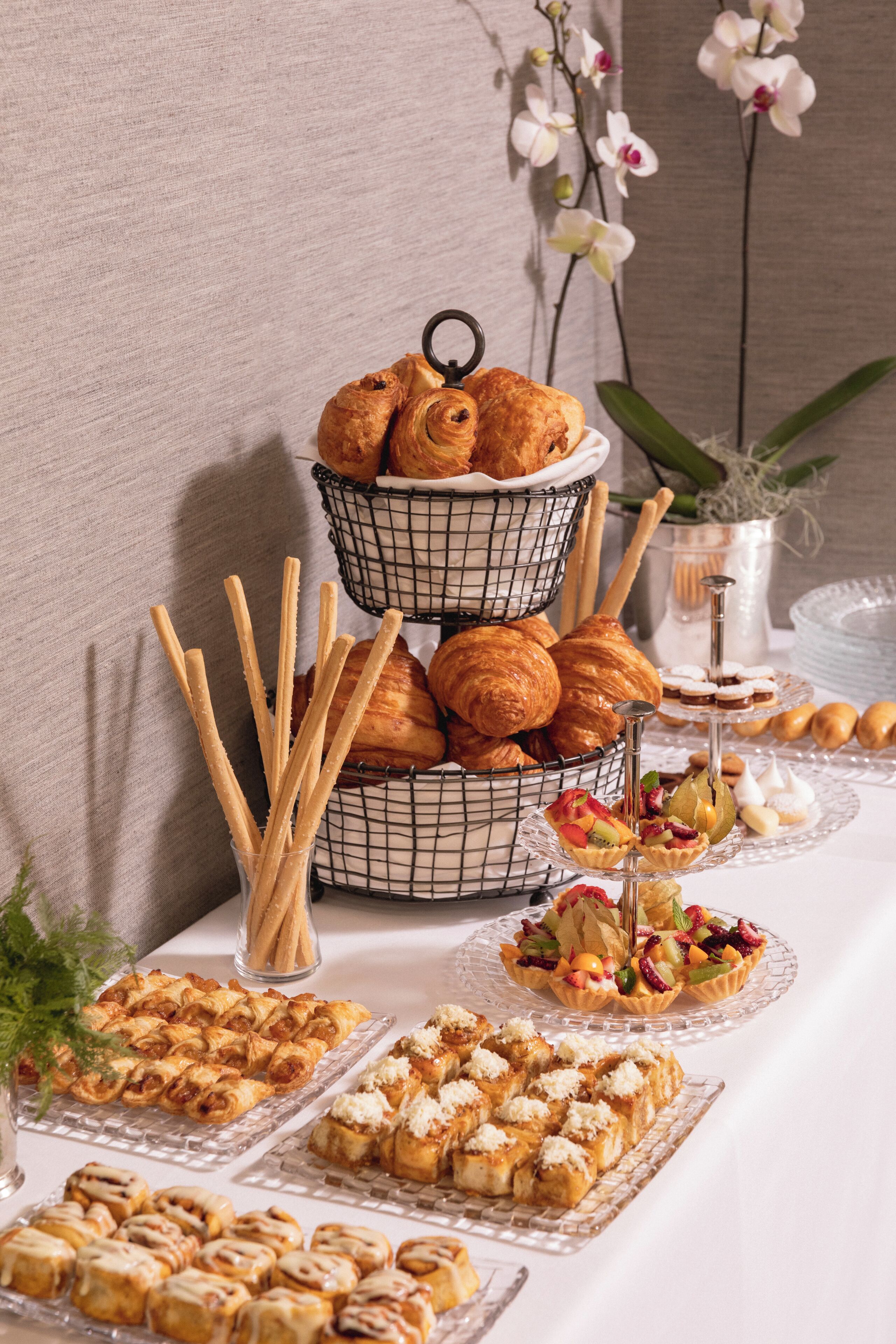 A buffet table with various pastries and desserts, including croissants, muffins, and fruit tarts.