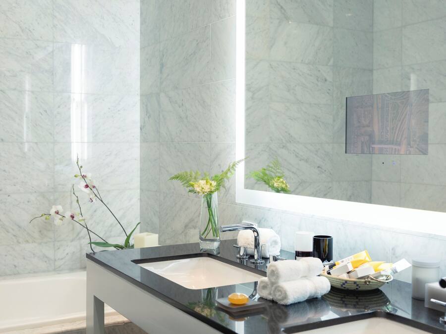 Une salle de bain moderne avec un mur en marbre, un plan de travail noir, un lavabo, un miroir et un vase rempli de fleurs.