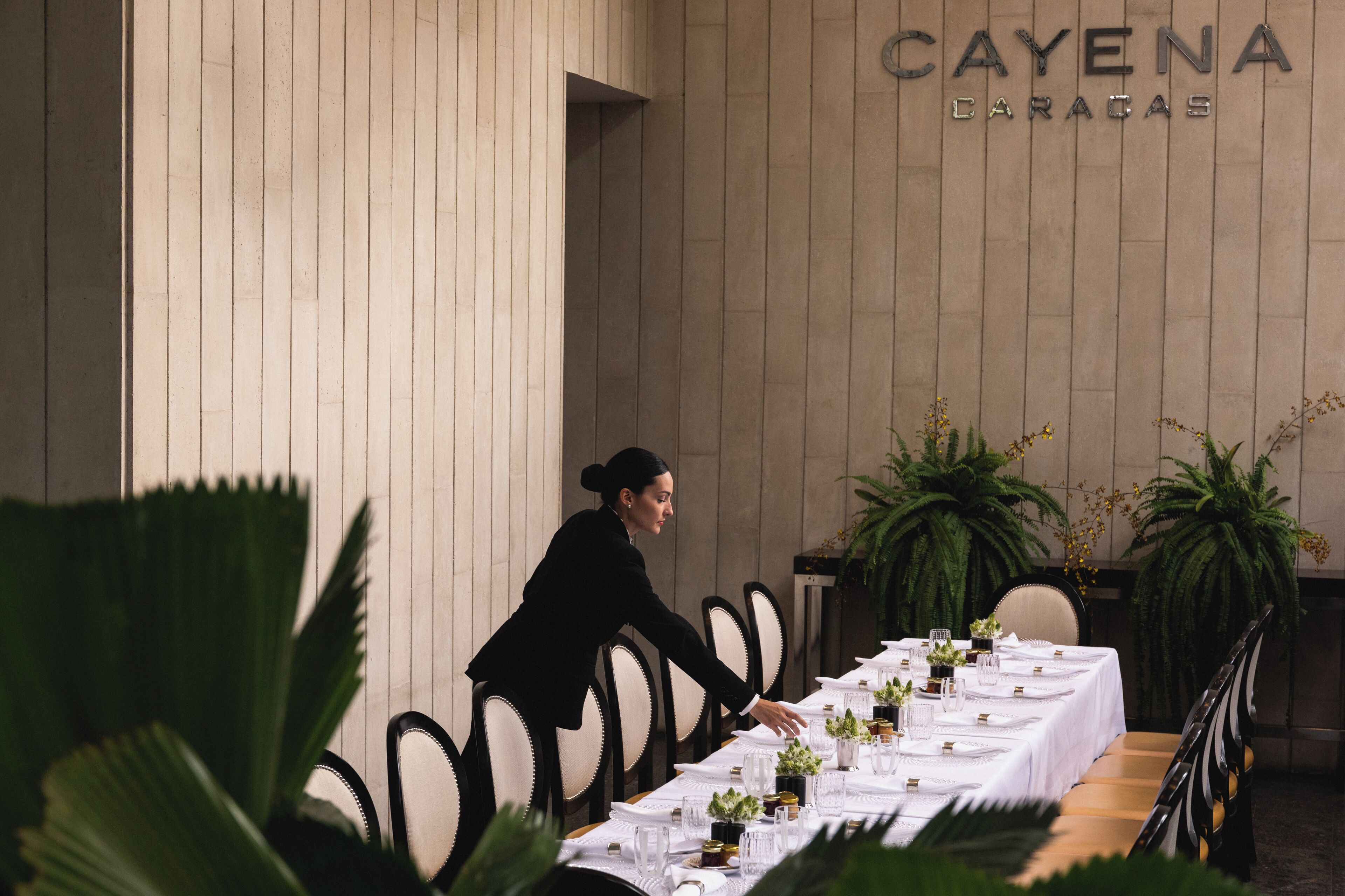 Uma mesa formal para refeições, longa, com cadeiras e um garçom.