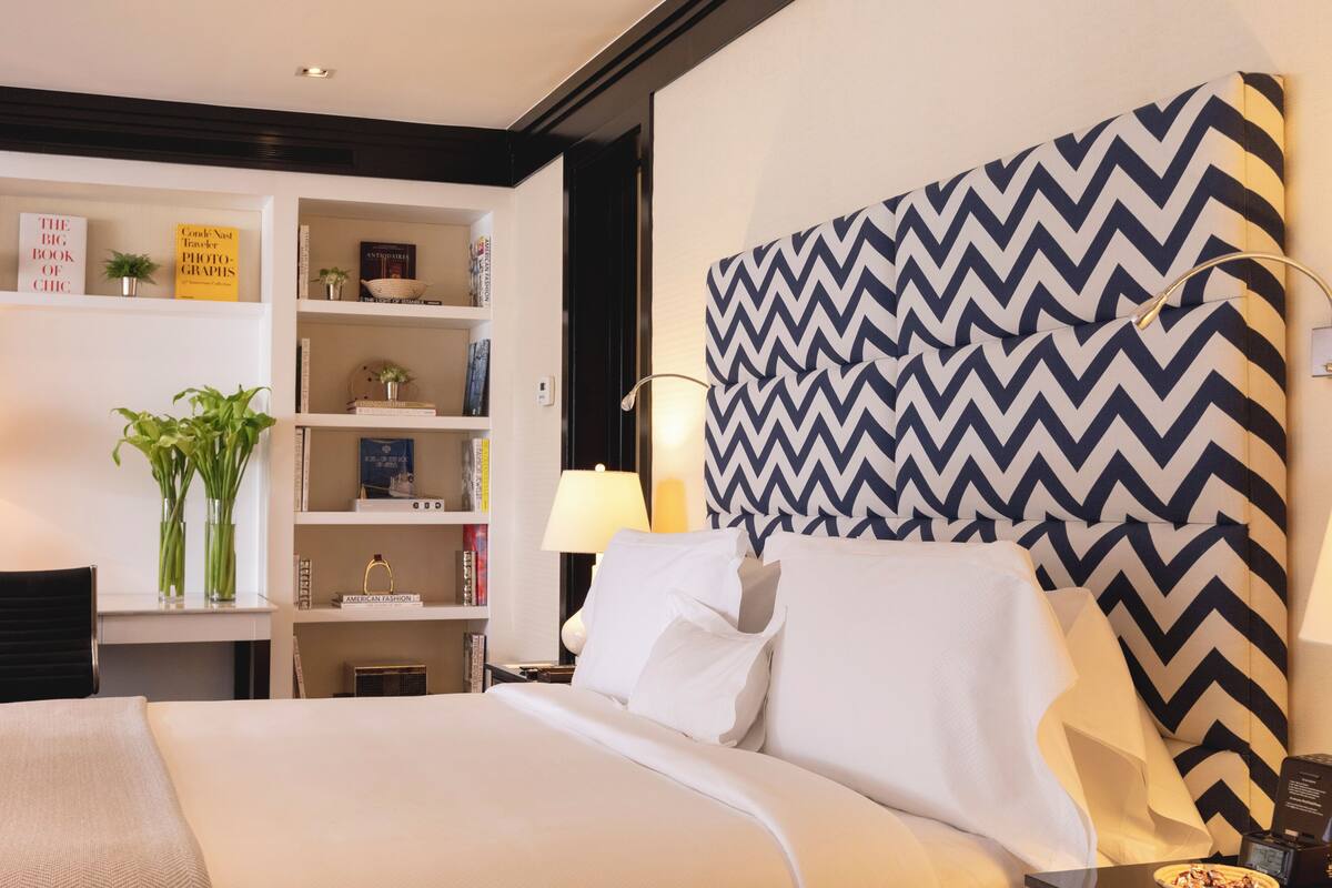 Une chambre d’hôtel comprenant un lit, une table de chevet, une lampe, une bibliothèque et un panneau décoratif mural.