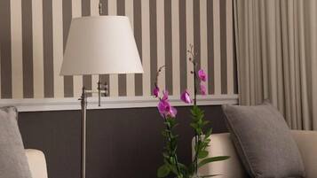 A modern hotel room with striped wallpaper, a lamp, a small table with a book, and a plant.