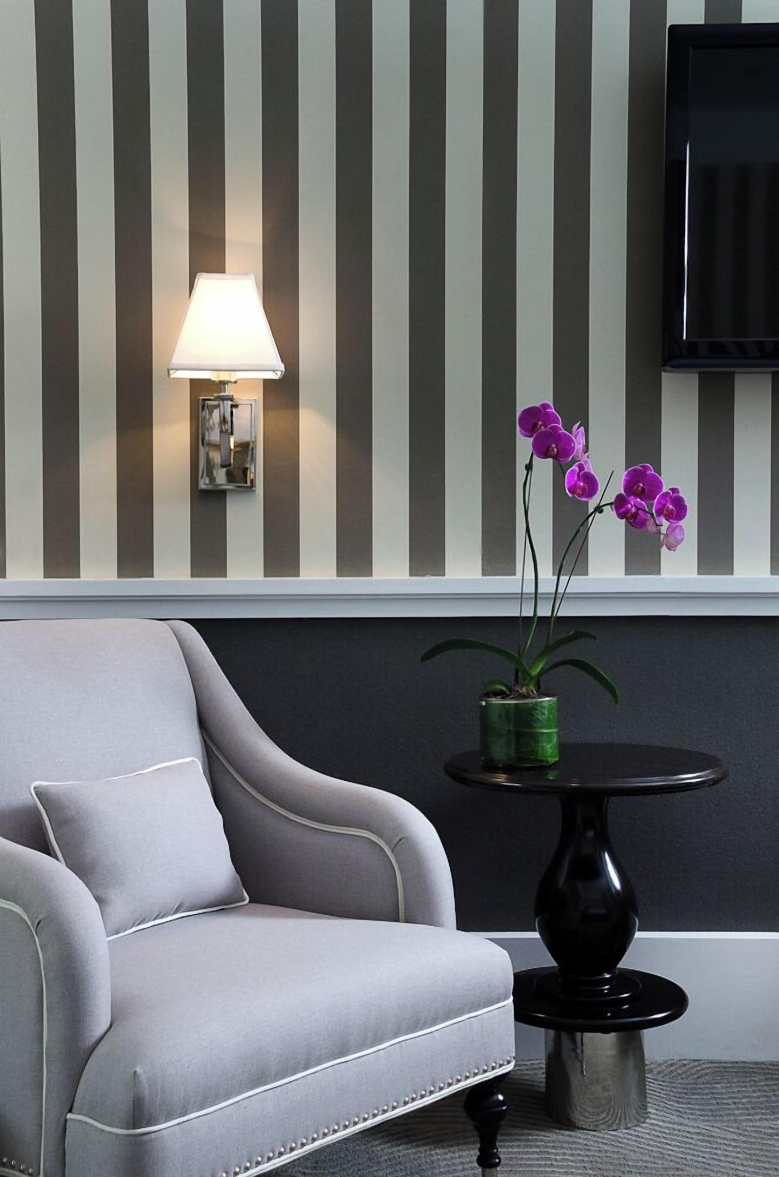 Ein modernes Zimmer mit einem grauen Sofa, einem kleinen runden Tisch mit einer Zimmerpflanze und einer Wandlampe.