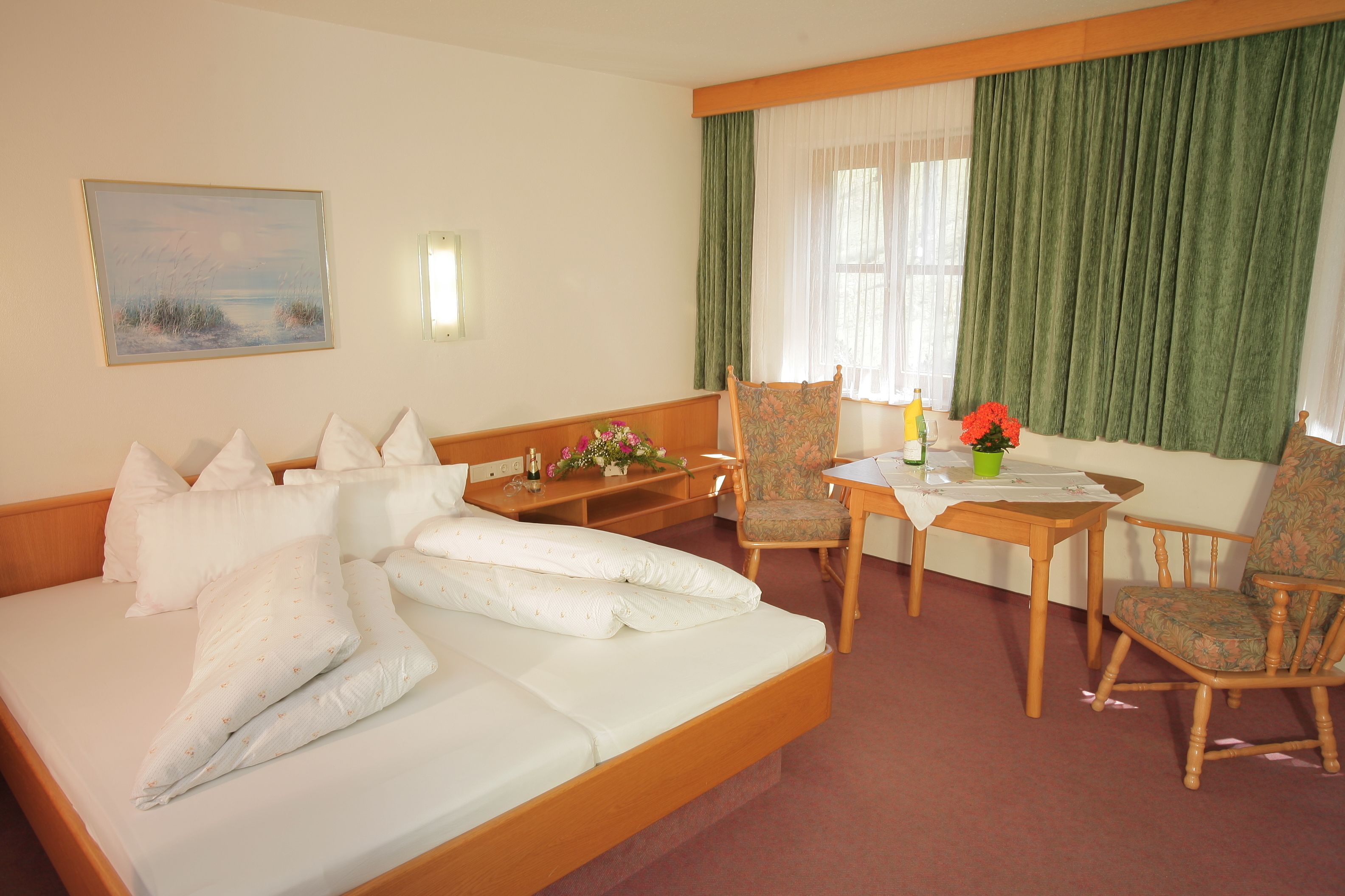 A hotel room with a bed, a desk, two chairs, a table, a lamp, and a painting on the wall.
