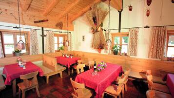 A rustic dining area with wooden tables and benches, decorated with red tablecloths and floral centerpieces.