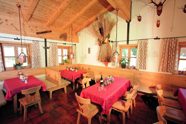 A rustic dining area with wooden tables and benches, decorated with red tablecloths and floral centerpieces.