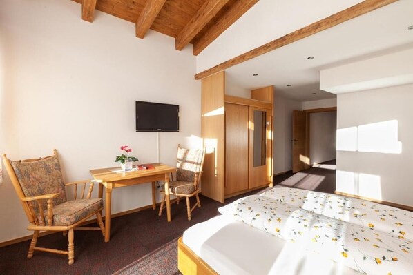 A hotel room with a wooden bed, a desk with a chair, a television, and a wardrobe.