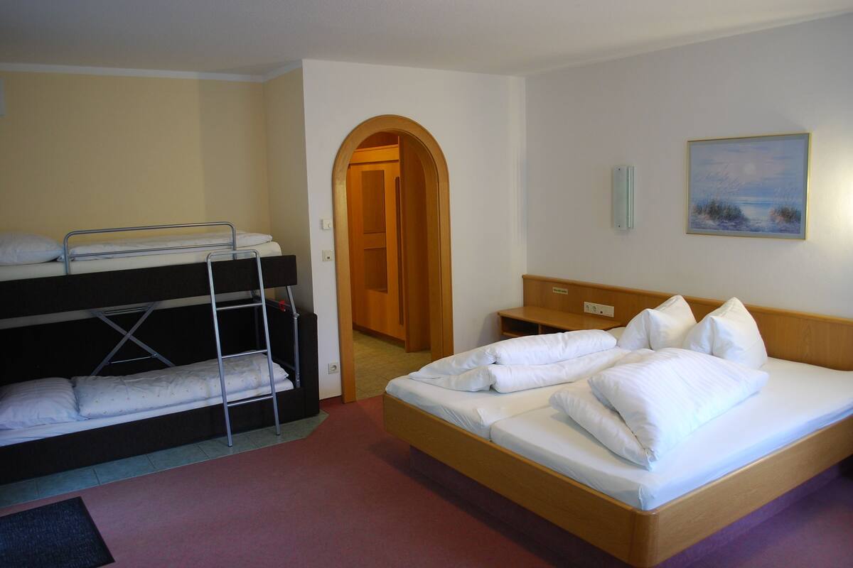 Ein Hotelzimmer mit Etagenbett, einem Einzelbett, einem hölzernen Kopfteil, einem Nachttisch und einem Bild an der Wand.