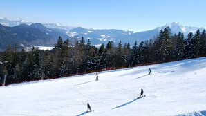 A snowy ski slope with skiers and a mountainous backdrop.