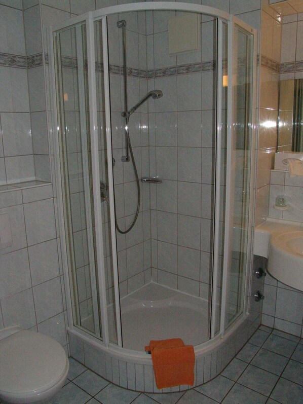 Ducha de esquina con puertas de cristal, inodoro y lavamanos.