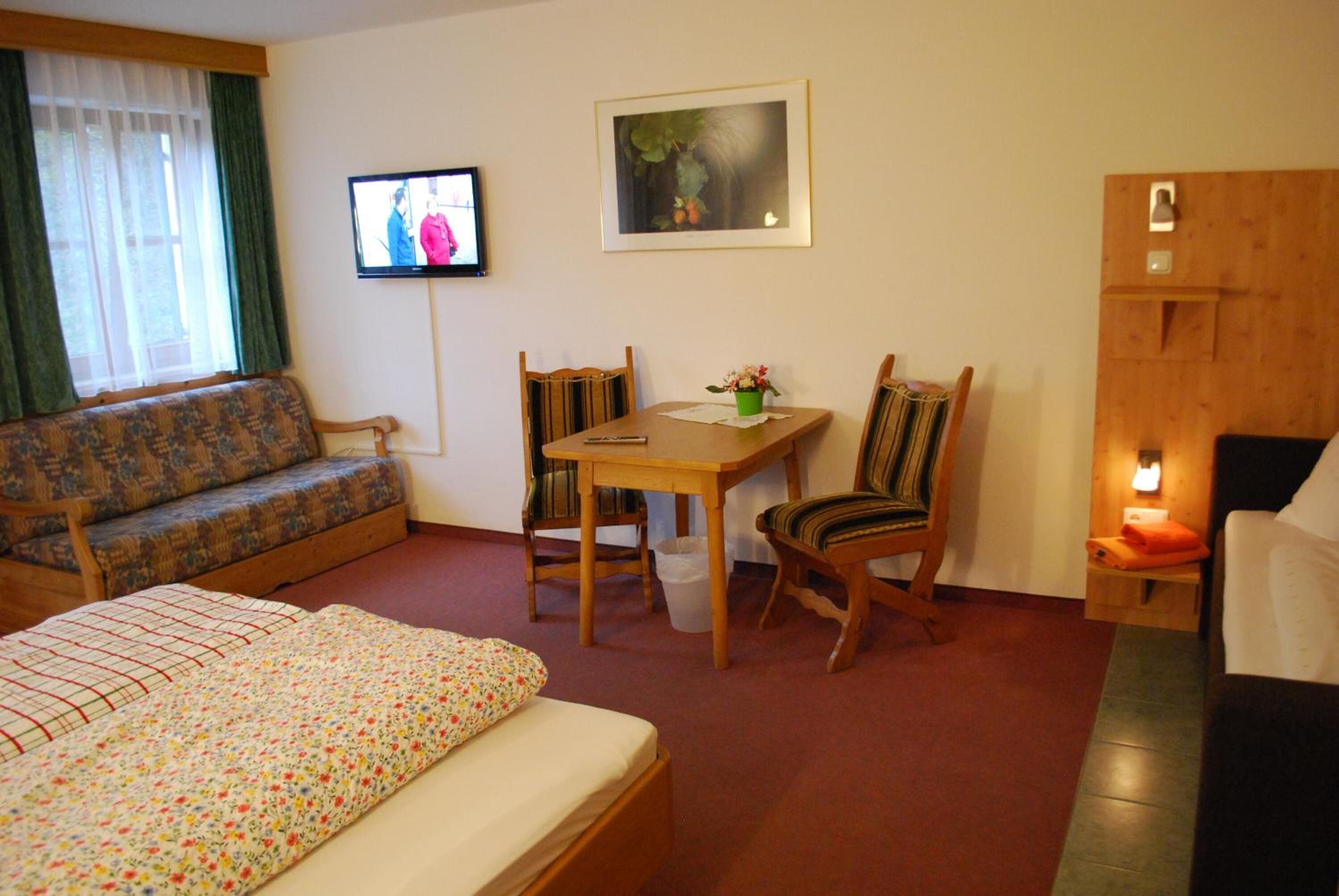 Ein gemütliches Zimmer mit einem Bett, einer Couch, einem kleinen Tisch mit Stühlen, einem Fernseher und einem gerahmten Bild an der Wand.