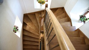 Un escalier en bois, doté d’une rampe, mène à un palier où se trouve un vase rempli de fleurs.
