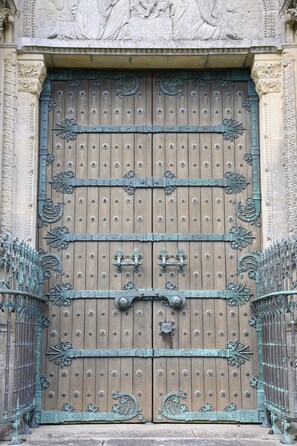 Een grote, versierde houten deur met gedetailleerd metaalwerk en een decoratief stenen reliëf erboven.