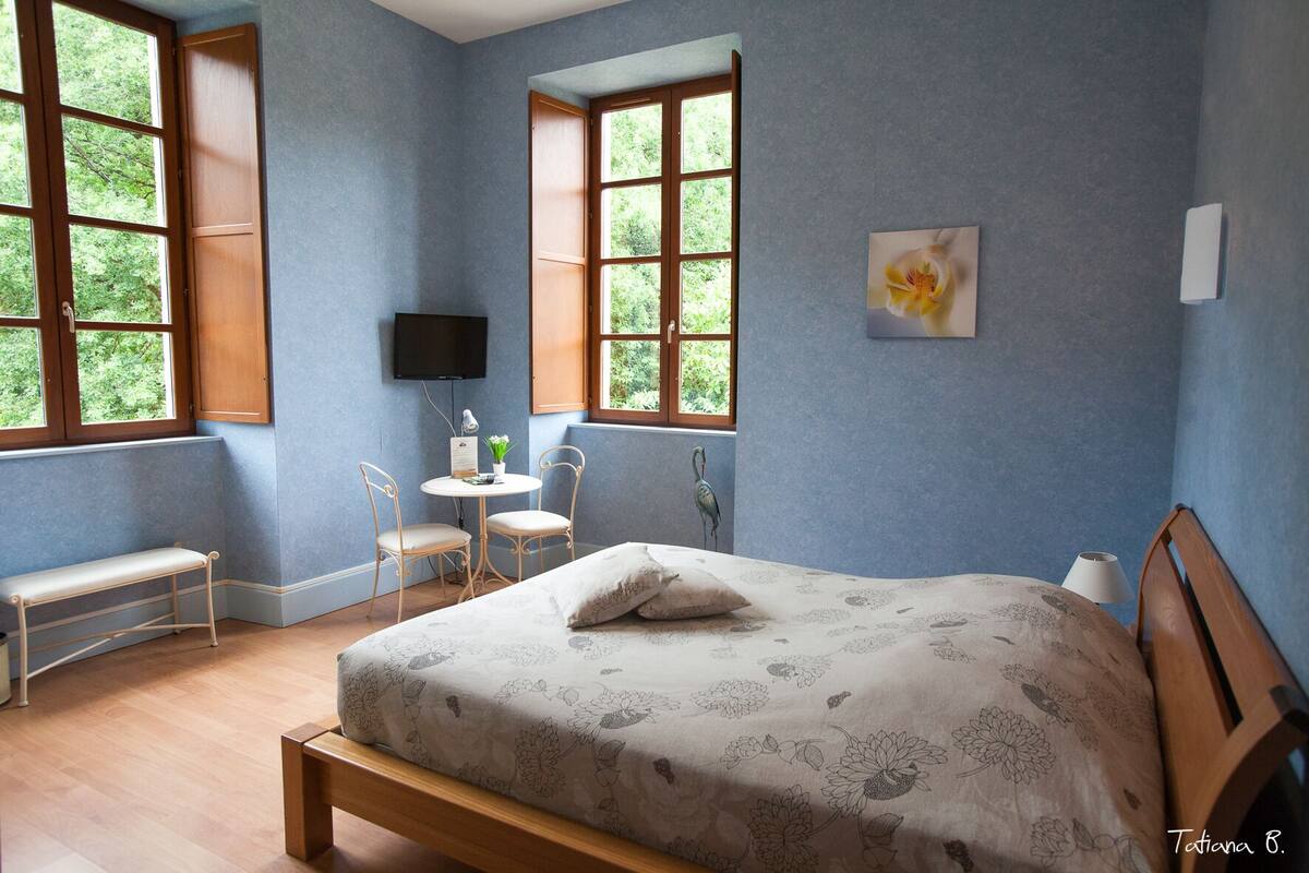 Ein Schlafzimmer mit einem Bett, einem Schreibtisch, zwei Stühlen, einer Bank, einem Fernseher und großen Fenstern.