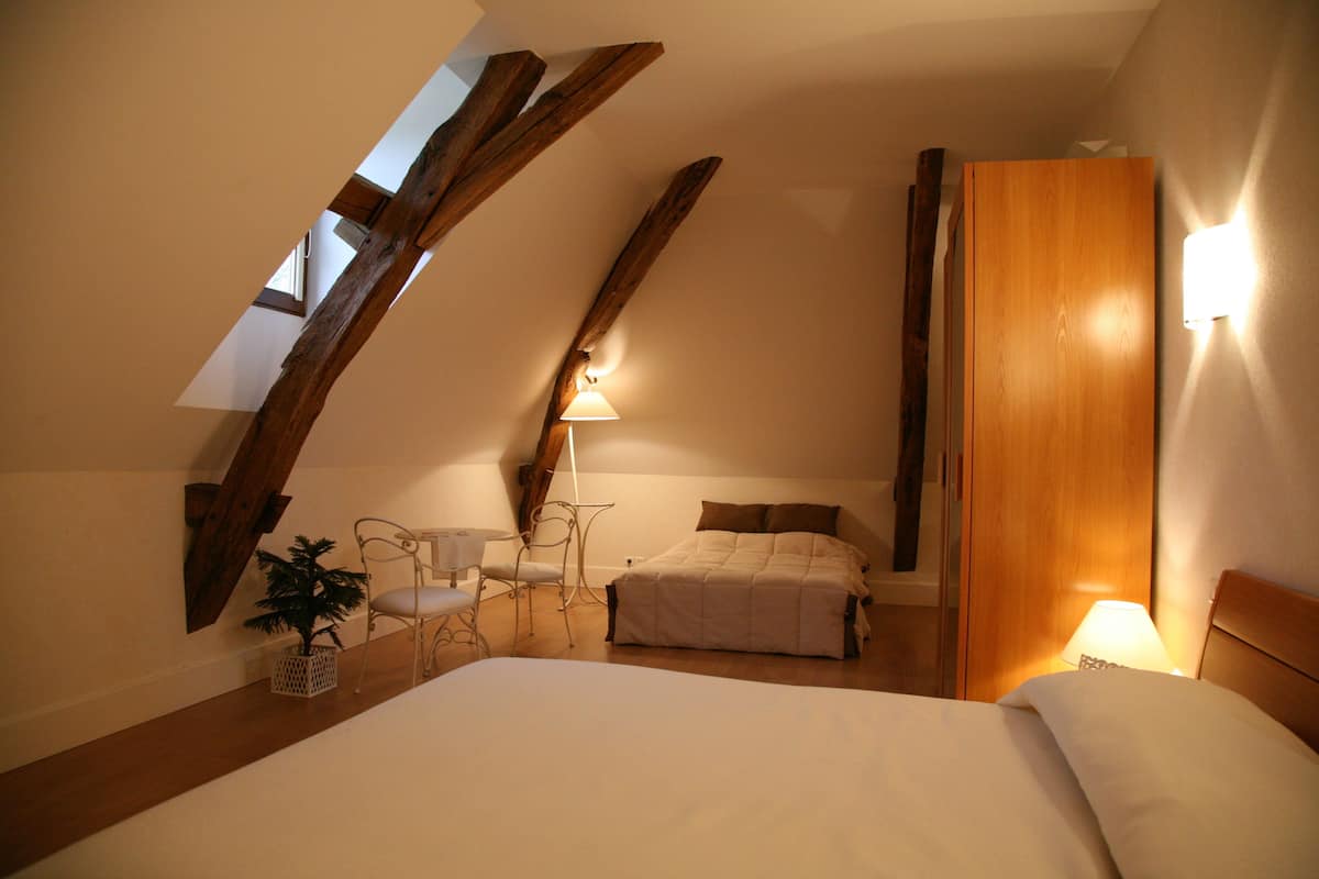 Ein Schlafzimmer mit schrägem Dach, einem Bett, einem Nachttisch, einem Sessel, einer Lampe und einem Holzschrank.