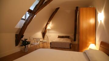 A bedroom with a sloped ceiling, a bed, a bedside table, a chair, a lamp, and a wooden wardrobe.