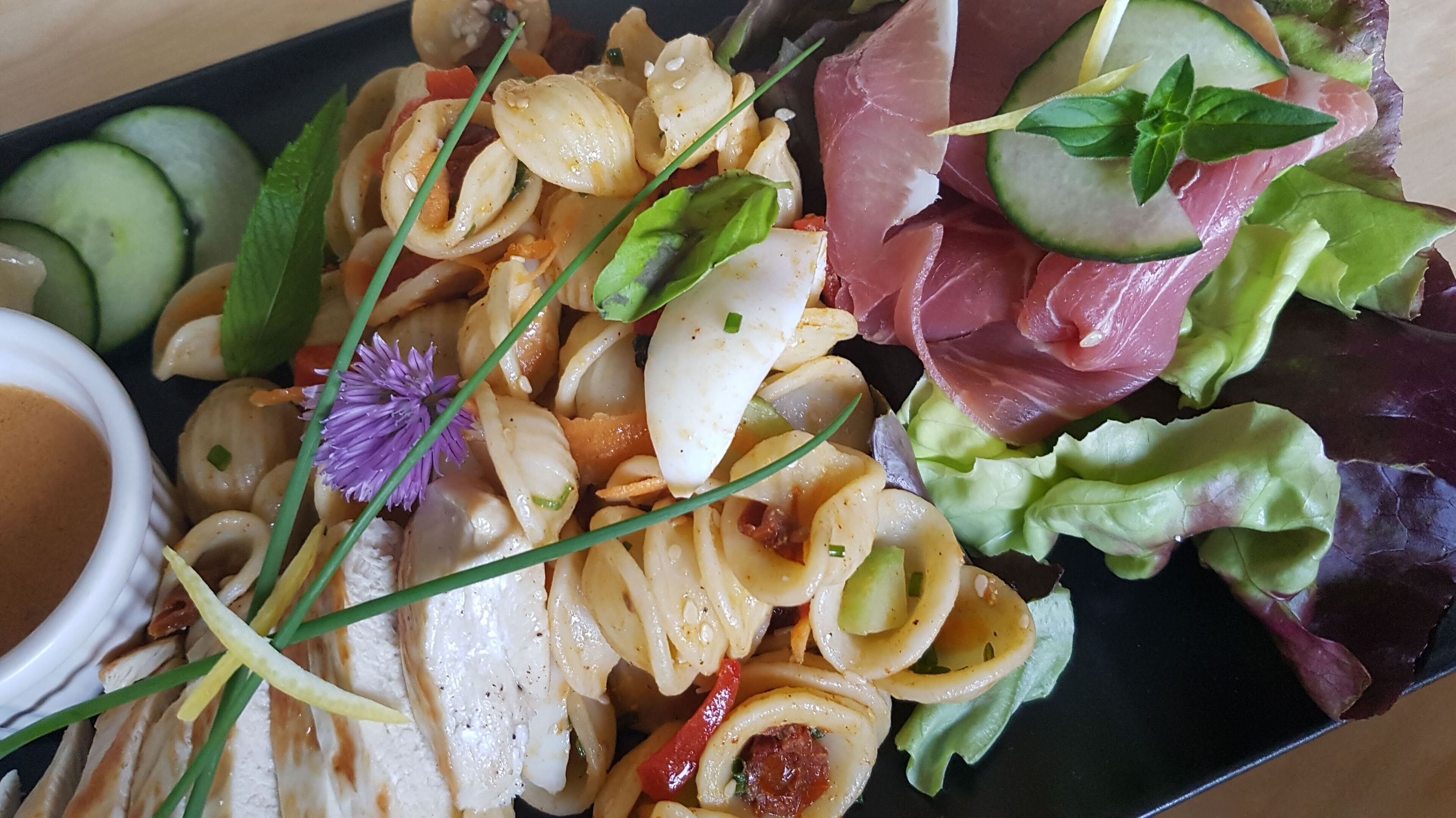 A plate of food with various ingredients including vegetables, meat, and a small bowl of sauce.