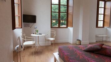 Een kamer met een bed, een bureau, twee stoelen, een televisie en een raam met uitzicht op bomen.
