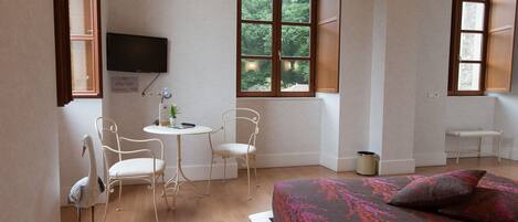 A room with a bed, a desk, two chairs, a television, and a window with a view of trees.