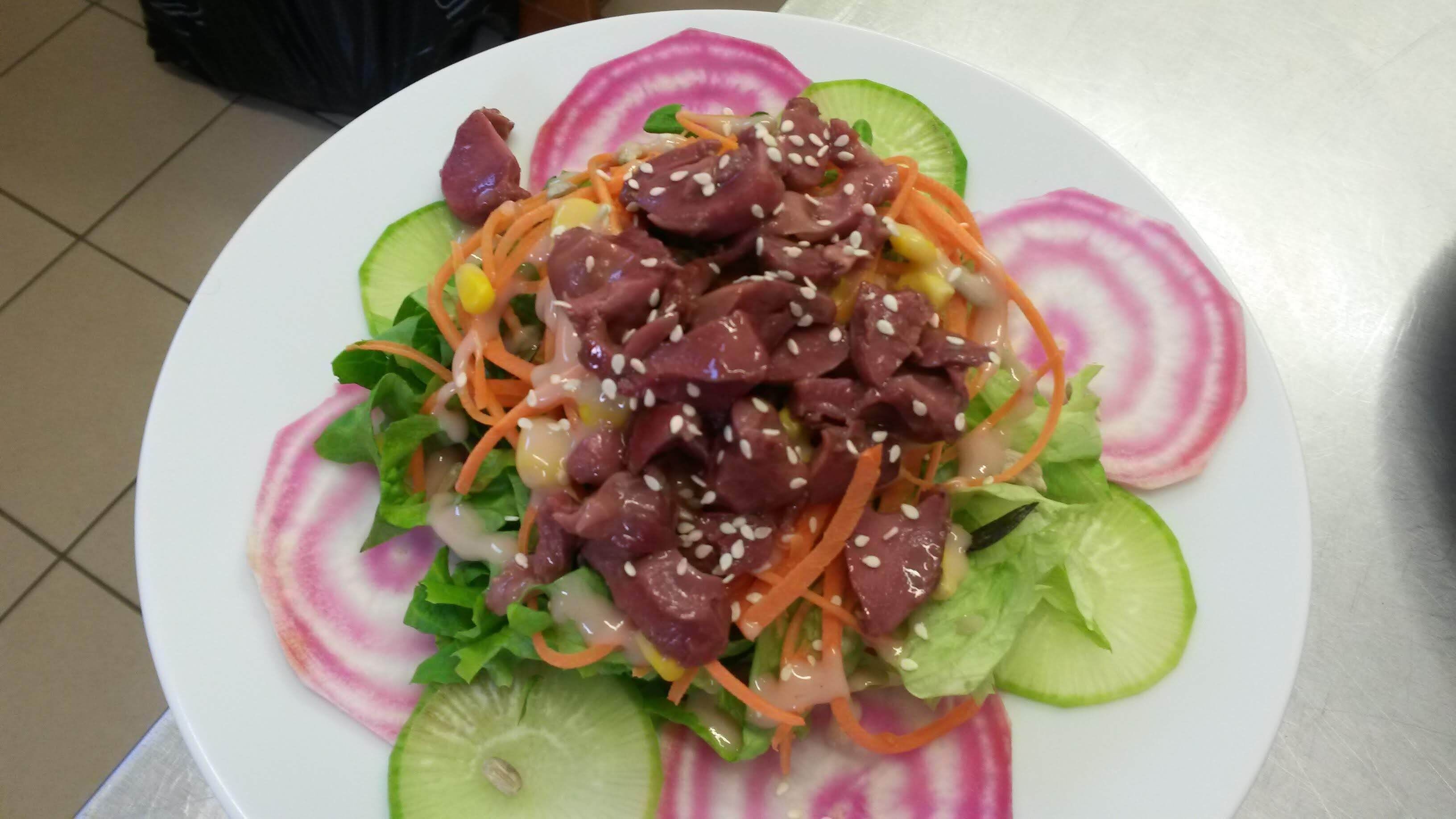 Une assiette de nourriture comprenant divers légumes et de la viande, garnie de graines de sésame.
