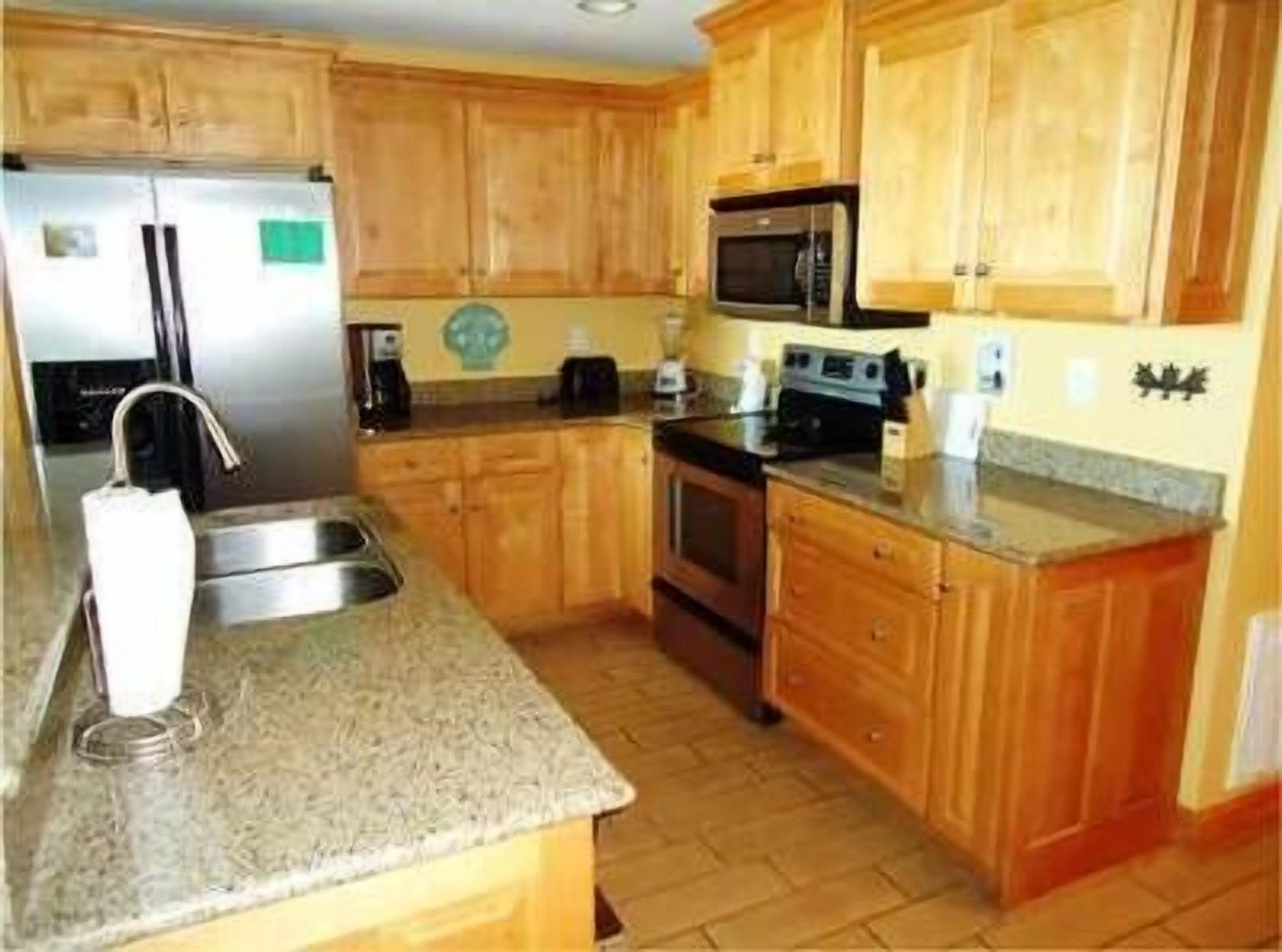 A kitchen with wooden cabinets, a stainless steel refrigerator, a microwave, and a stove.