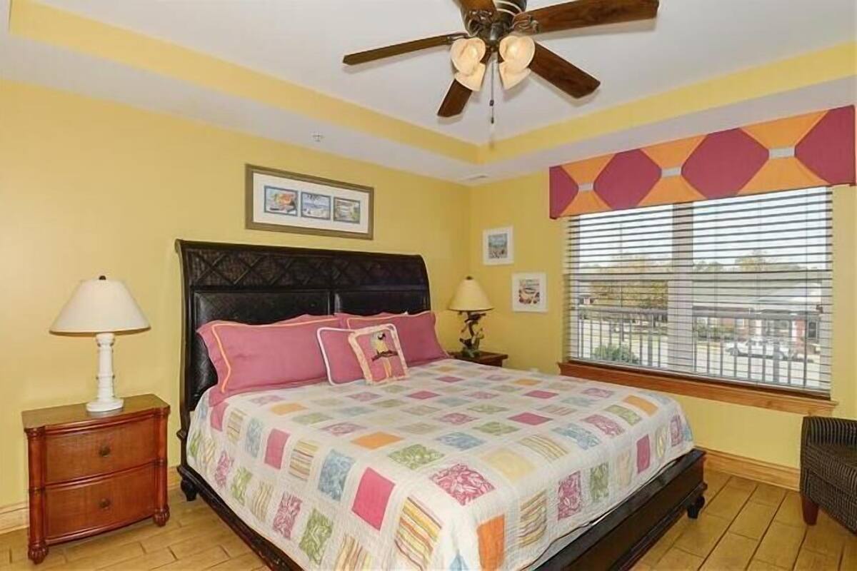 A bedroom with a bed, two bedside tables, a ceiling fan, and a window with blinds.