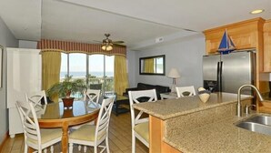 Une cuisine compacte avec un îlot central, un coin repas avec une table ronde et des chaises, et un balcon agrémenté de rideaux.