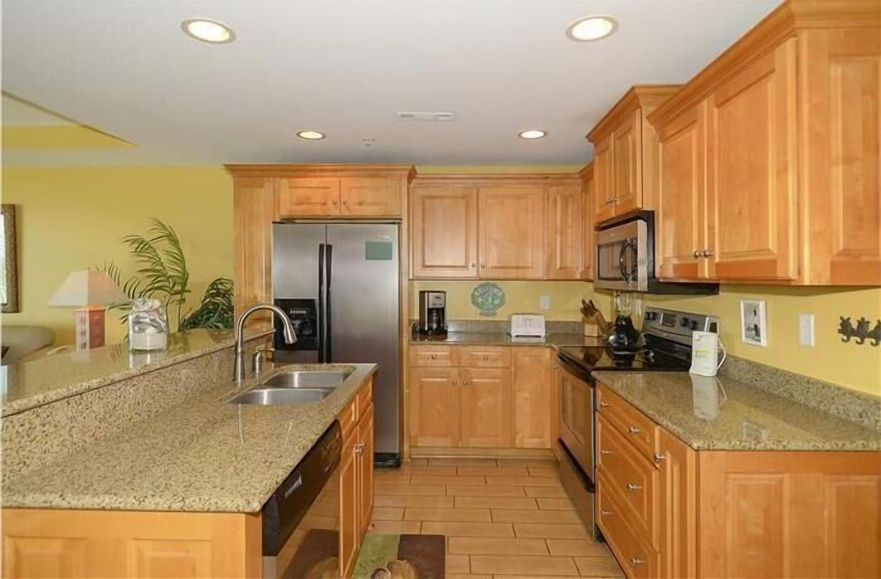 A kitchen with wooden cabinets, granite countertops, a refrigerator, a microwave, and a stove.