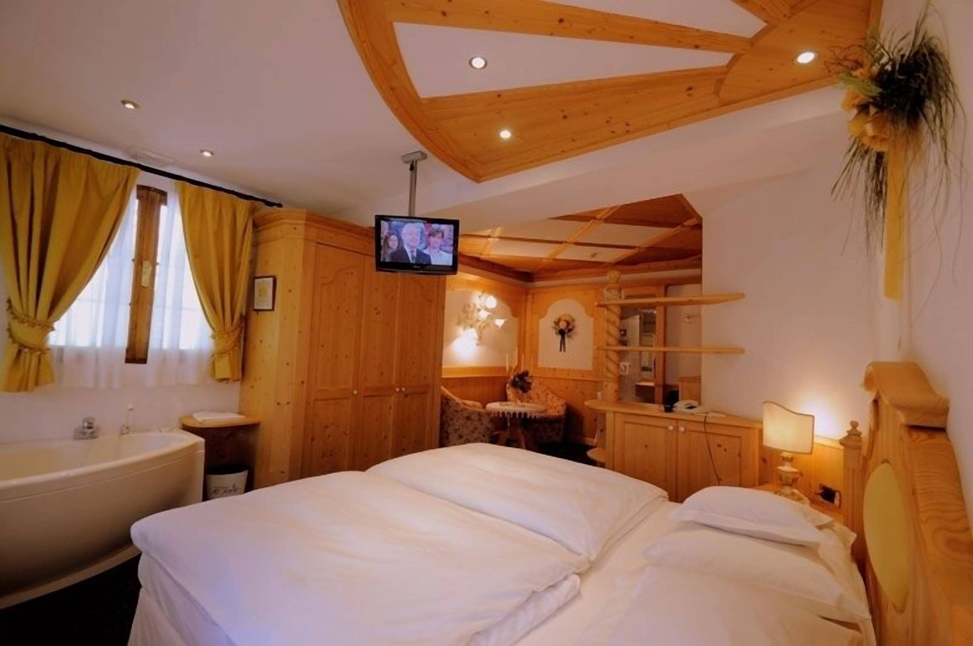 Une chambre à coucher meublée en bois, avec un grand lit, une télévision et une salle de bain équipée d’une baignoire.