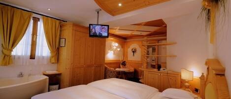 Une chambre à coucher meublée en bois, avec un grand lit, une télévision et une salle de bain équipée d’une baignoire.