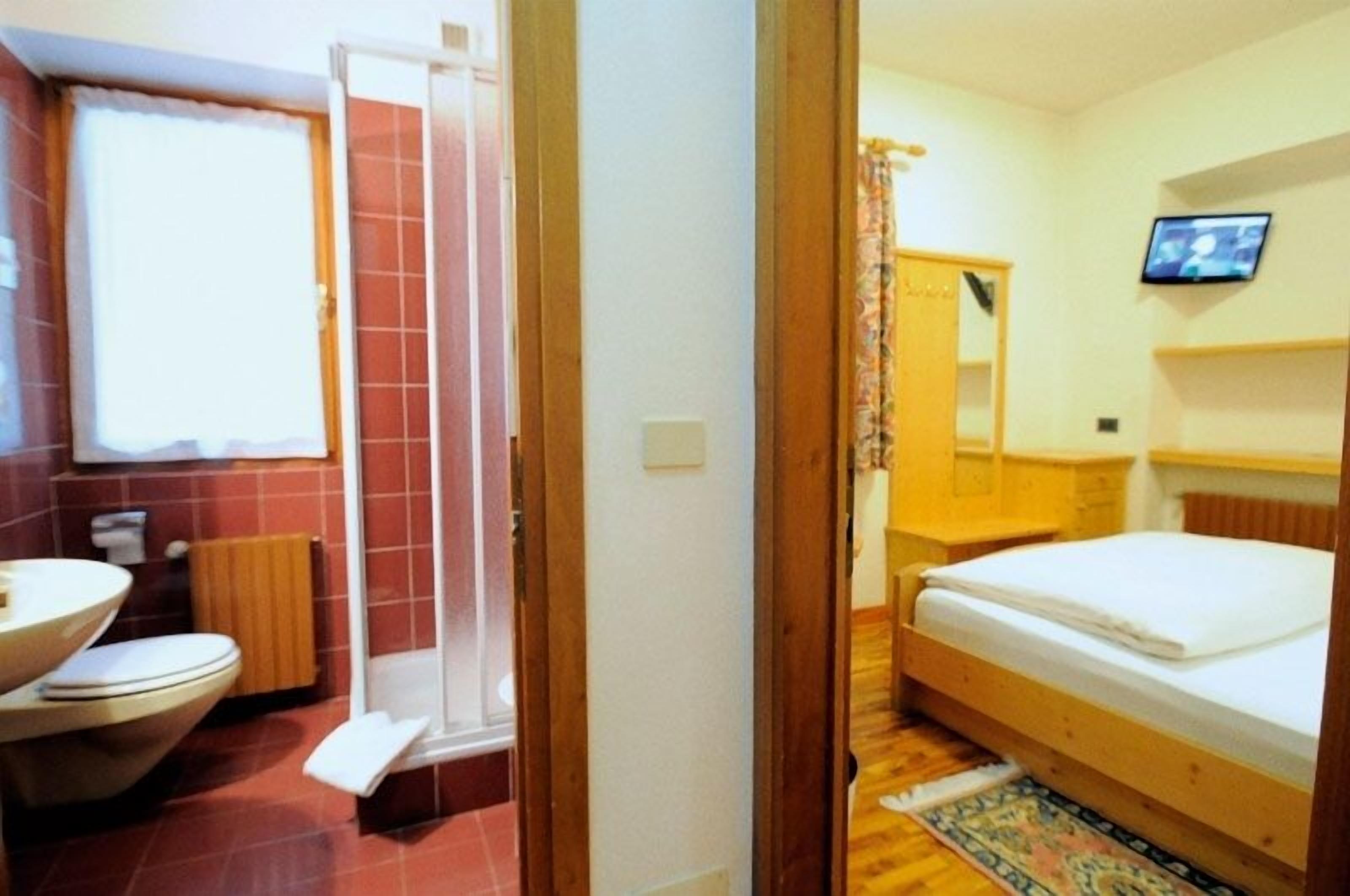 Une chambre avec un lit en bois, une petite table de chevet, un miroir et un téléviseur fixé au mur.