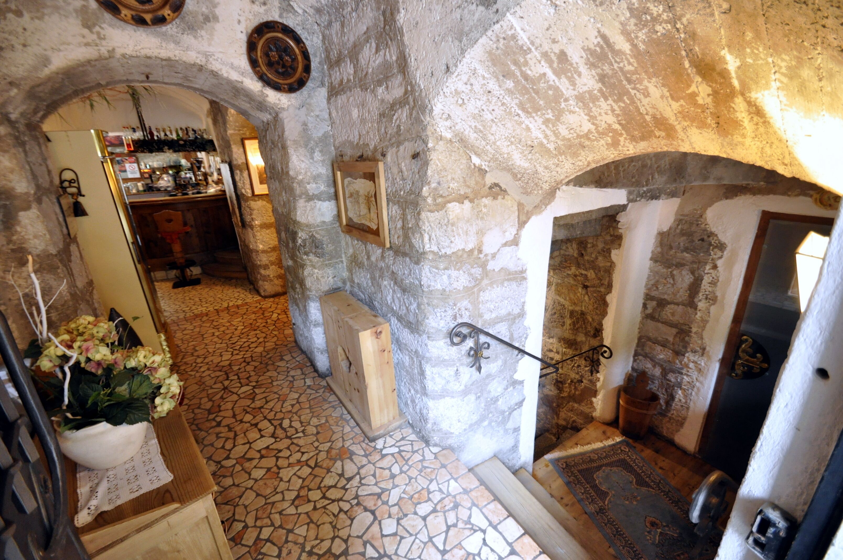 A narrow stone corridor with a tiled floor, a wooden chest, and a small wooden table with a plant.