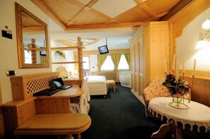 A cozy room with a wooden ceiling, a bed, a desk with a laptop, a small table with candles, and a TV on the wall. - Hotel Al Forte (Livinallongo del Col di Lana)