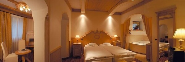 A hotel room with a large bed, two bedside tables with lamps, a mirror, and a small round table with a chair. - Hotel Al Forte (Livinallongo del Col di Lana)