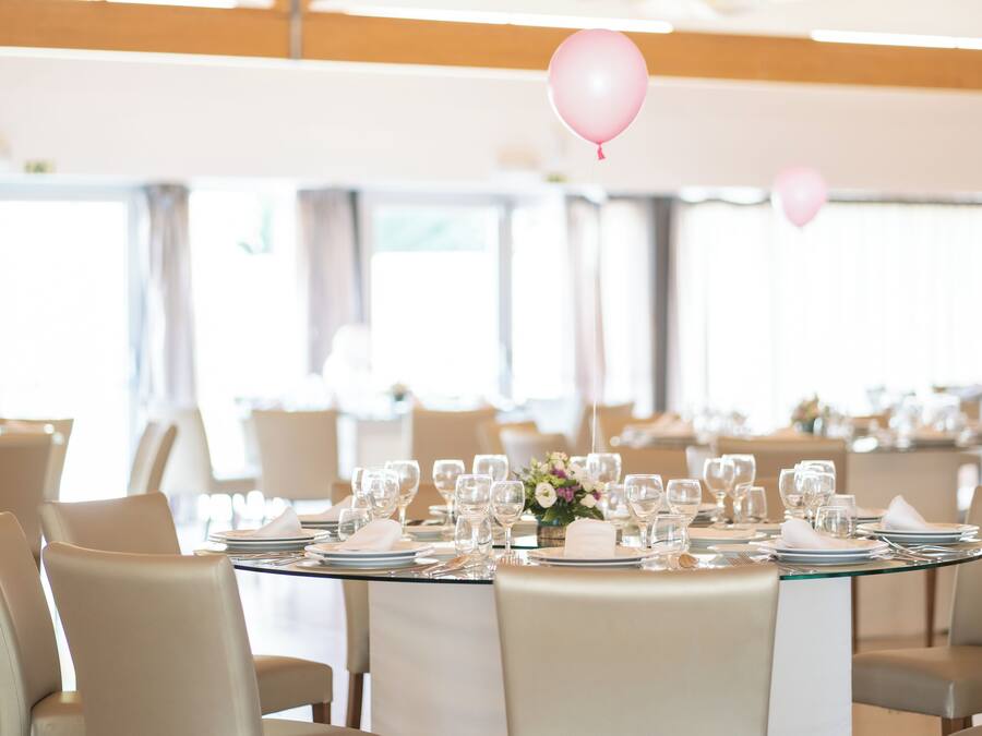 A dining area with round tables set for a meal, featuring white linens and clear glassware.