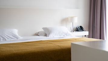 A hotel room with a bed, a bedside table with a lamp, a phone, and a window with curtains.
