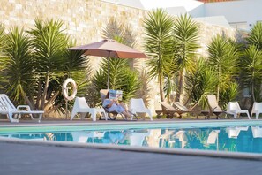 A poolside area with lounge chairs, a pool, and palm trees. - Vila D'Obidos (Obidos)