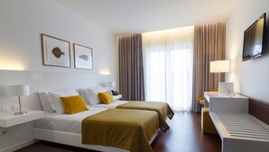 Ein Hotelzimmer mit zwei Betten, einem Schreibtisch, einem Fernseher und einem Fenster mit Vorhängen.