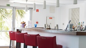 Eine moderne Bar mit einer Holztheke, roten Barhocker und Pendelleuchten.