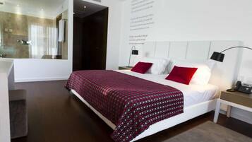 A modern hotel room with a large bed, a bedside table with a lamp, and a mirror on the wall.