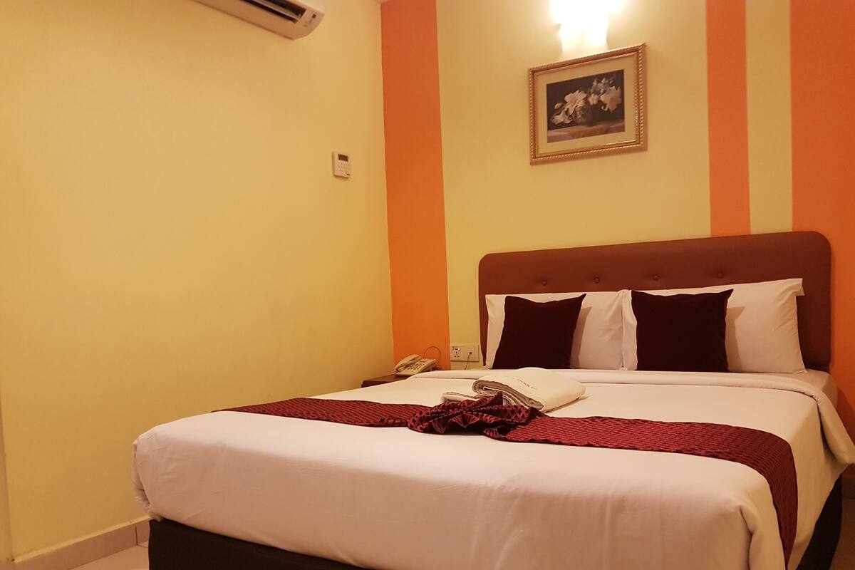 A hotel room with a bed, a telephone, and a wall-mounted air conditioner.